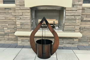 Modern outdoor fire pit with decorative plant holder against a stone wall.